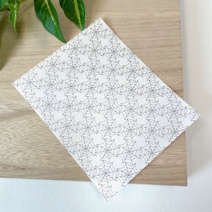 May include: A white sheet of paper with a black and white spiderweb pattern. The paper is on a light brown wooden surface.