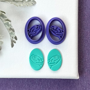 May include: Two pairs of lizard-shaped cookie cutters. One pair is purple and the other pair is teal.