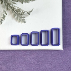 May include: Five purple plastic rectangle cookie cutters of varying sizes, arranged in order from smallest to largest.
