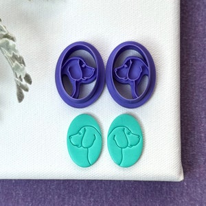 May include: Two purple plastic dog head cookie cutters and two teal blue dog head cookies.