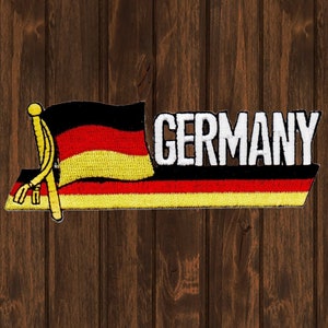 May include: A black, red, and yellow embroidered patch with the word "GERMANY" in white letters. The patch features a stylized German flag with a gold tassel.