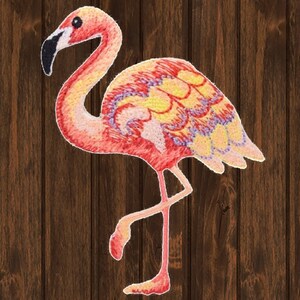 May include: Pink flamingo embroidered patch with yellow, orange, and purple details. The flamingo is standing on one leg with its neck curved.