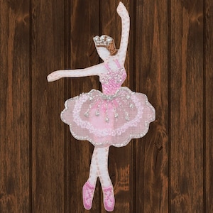 May include: Pink ballerina applique with a silver glitter tutu and a crown. The ballerina is in a dancing pose with her arms raised above her head.