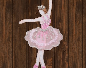 Op de afbeelding: Roze ballerina applicatie met een zilveren glitter tutu en een kroon. De ballerina staat in een danspose met haar armen boven haar hoofd.