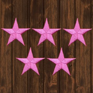 May include: Five pink fabric star-shaped patches on a brown wooden background.