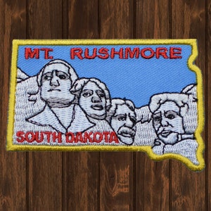 May include: Embroidered patch featuring a blue sky with the text "MT. RUSHMORE" in red and "SOUTH DAKOTA" in red. The patch depicts the four presidents carved into Mount Rushmore: George Washington, Thomas Jefferson, Theodore Roosevelt, and Abraham Lincoln.