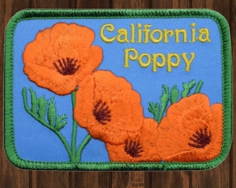May include: Embroidered patch featuring three orange California poppies on a blue background with green stems and leaves. The patch has a green border and the text "California Poppy" in yellow thread.