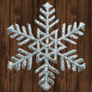 Könnte beinhalten: Eine silberne Schneeflocke mit einem detaillierten, komplizierten Design. Die Schneeflocke befindet sich vor einem Holzmaserungshintergrund.