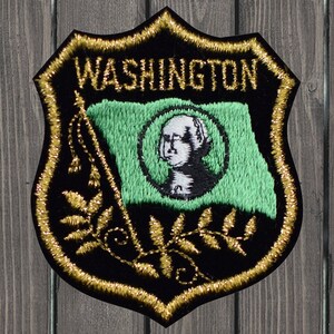 May include: A black and gold embroidered patch with the word "WASHINGTON" in gold lettering. The patch features a green flag with a white portrait of George Washington in a circle.