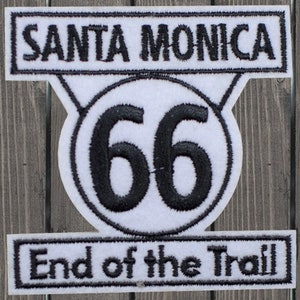 Puede incluir: Parche bordado blanco y negro con el texto "Santa Monica" en la parte superior, un círculo blanco con el número "66" en negro y el texto "End of the Trail" en la parte inferior.