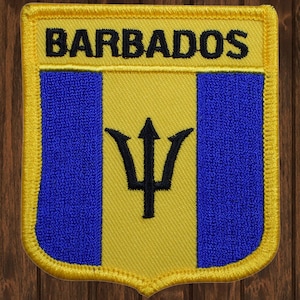 Könnte beinhalten: Ein gestickter Aufnäher in Gelb, Blau und Schwarz mit dem Wort "BARBADOS" in schwarzen Buchstaben. Der Aufnäher zeigt die Nationalflagge von Barbados, die ein gelbes Feld mit einem blauen vertikalen Streifen auf jeder Seite und einem schwarzen Dreizack in der Mitte enthält.