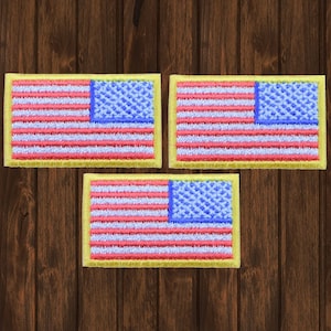 Może przedstawiać: Trzy haftowane naszywki z amerykańską flagą z żółtą obwódką. Flagi są czerwone, białe i niebieskie z niebieskim polem gwiazd.