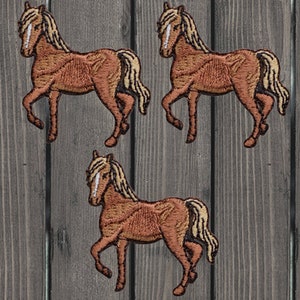 Puede incluir: Tres parches de caballo bordados de color marrón con una crin y una cola de color marrón claro. Los caballos están de pie sobre sus patas traseras con las patas delanteras levantadas.