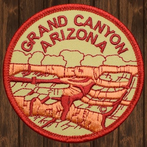 May include: Embroidered patch featuring the Grand Canyon in Arizona. The patch has a circular shape with a red border and text. The design includes a detailed depiction of the canyon's landscape in shades of orange and red.