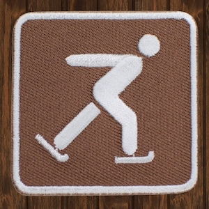 May include: A brown square patch with a white outline and a white figure ice skating. The figure is stylised and has a simple design.