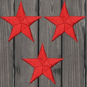 Puede incluir: Tres estrellas rojas bordadas sobre un fondo de vetas de madera oscura. Cada estrella tiene cinco puntas y una textura cosida detallada. Las estrellas están espaciadas uniformemente, creando una disposición visualmente atractiva.