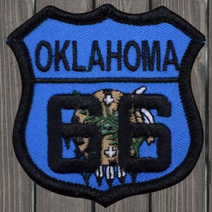 May include: A blue and black embroidered patch with the text "OKLAHOMA" and the number "66" inside a shield shape. The number "66" is surrounded by a stylized image of the state of Oklahoma.