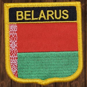 Może przedstawiać: Naszywka haftowana z flagą Białorusi, z napisem "BELARUS" w żółtych literach na czarnym tle.