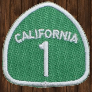 May include: Green and white California Highway 1 patch. The patch is shaped like a rounded triangle with a white border and the text "CALIFORNIA 1" in white.