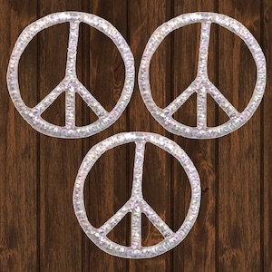 May include: Three silver peace sign stickers with a sparkly finish. The stickers are on a brown wooden background.