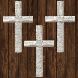 Puede incluir: Tres cruces plateadas con purpurina sobre un fondo de madera marrón.