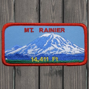 May include: Red, white and blue embroidered patch featuring a mountain scene and the text "MT. RAINIER 14,411 Ft."