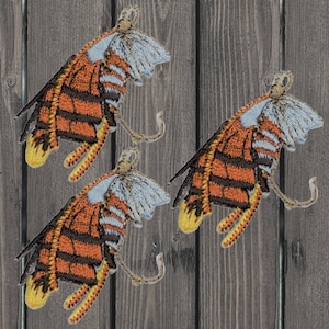 Peut inclure: Trois écussons brodés en forme de papillon de nuit avec des ailes orange, noires et jaunes, et une tête bleu clair et blanche. Les écussons ont un design incurvé en forme d'antenne. Le fond est une surface en bois.