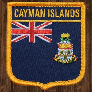 May include: A blue and yellow embroidered patch with the text "CAYMAN ISLANDS" and the Cayman Islands flag. The flag features a Union Jack in the upper left corner and the coat of arms in the lower right corner.