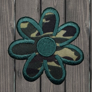 May include: A green and brown camouflage patterned fabric flower with a teal outline. The flower has six petals and a center circle.