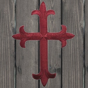 Pode incluir: Uma cruz vermelha com um design decorativo e ornamentado. A cruz está sobre um fundo de madeira.
