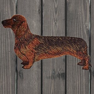 May include: A brown and black embroidered dachshund silhouette patch. The patch is made of fabric and has a textured surface.