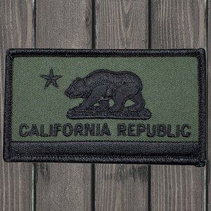 Puede incluir: Un parche bordado en negro y verde con el texto "CALIFORNIA REPUBLIC" y una silueta de oso negro con una estrella encima.