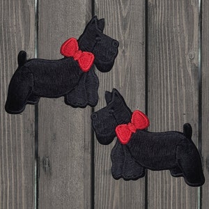 May include: Two black felt patches of Scottish Terrier dogs with red bow ties. The dogs are facing right and are in a walking position.