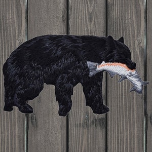 May include: Black bear silhouette with a fish in its mouth. The bear is walking to the right. The fish is orange and white.