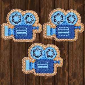 Op de afbeelding: Drie blauwe en gouden geborduurde strijk-op patches in de vorm van vintage filmcamera's.