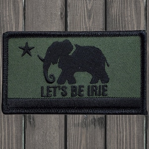 Peut inclure: Un patch brodé vert et noir avec une silhouette d'éléphant et le texte "LET'S BE IRIE".