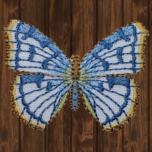 Könnte beinhalten: Ein detaillierter, gestickter Schmetterling mit blau-weißen Flügeln, die goldfarben umrandet sind. Der Körper des Schmetterlings ist eine Mischung aus Gold und Braun. Der Hintergrund ist eine dunkle Holzmaserung.
