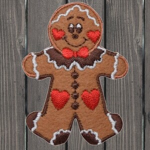 May include: A brown gingerbread man with white icing and red hearts. He is wearing a red bow tie.
