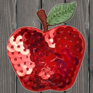 Puede incluir: Una manzana roja hecha de lentejuelas con una hoja verde en la parte superior. La manzana es un parche decorativo.
