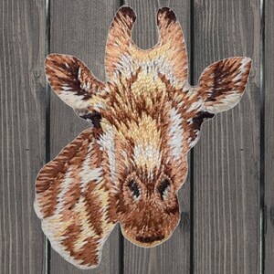 May include: Embroidered patch of a giraffe's head with brown and white markings. The giraffe's head is facing the viewer with its ears perked up.