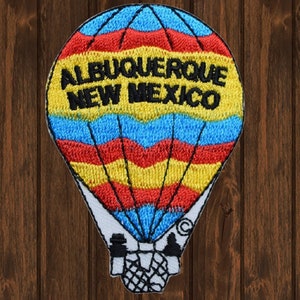 May include: Embroidered patch of a hot air balloon with red, yellow, and blue stripes. The balloon has the text "Albuquerque New Mexico" in black.