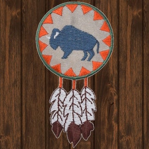 May include: A round, orange and green dreamcatcher with a blue embroidered buffalo in the center. The dreamcatcher has white feathers hanging from the bottom.