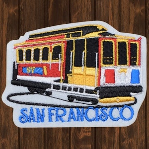May include: Embroidered patch featuring a red, yellow, and black San Francisco cable car with the text "SAN FRANCISCO" in blue lettering.