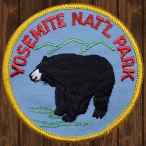 May include: A blue and yellow embroidered patch with the text "Yosemite National Park" in red. A black bear is in the center of the patch.