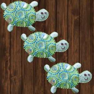 May include: Three green and blue embroidered turtle appliques with sequins. Each turtle has a smiling face.