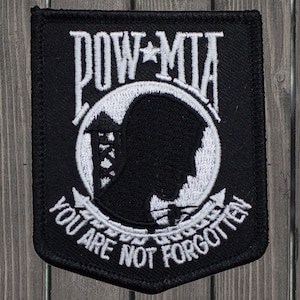 Può includere: Toppa ricamata in bianco e nero con le parole "POW*MIA You Are Not Forgotten". La toppa presenta una silhouette di una testa di soldato all'interno di un cerchio.