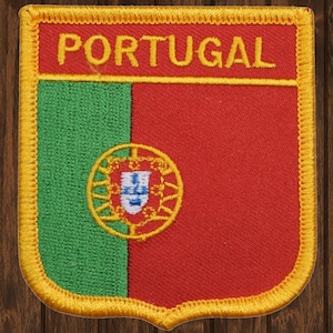 May include: A red, green, and yellow embroidered patch with the word "PORTUGAL" in yellow lettering. The patch features the Portuguese coat of arms in the center.