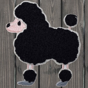 Puede incluir: Parche de caniche negro con contorno blanco. El caniche tiene cara y patas rosas. El parche está hecho de un material texturizado y está de pie.