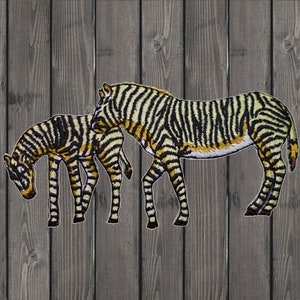 May include: Two black and white striped zebra figures, one larger than the other, are standing side-by-side on a woodgrain background.