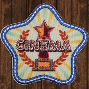 May include: A star-shaped patch with a blue border and a white background. The patch features a gold star on top of a brown trophy with the word "CINEMA" in brown letters.